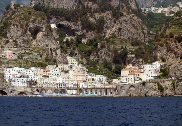 Atrani beach club nestled below dramatic cliffs, with colorful buildings cascading down to the sea.
