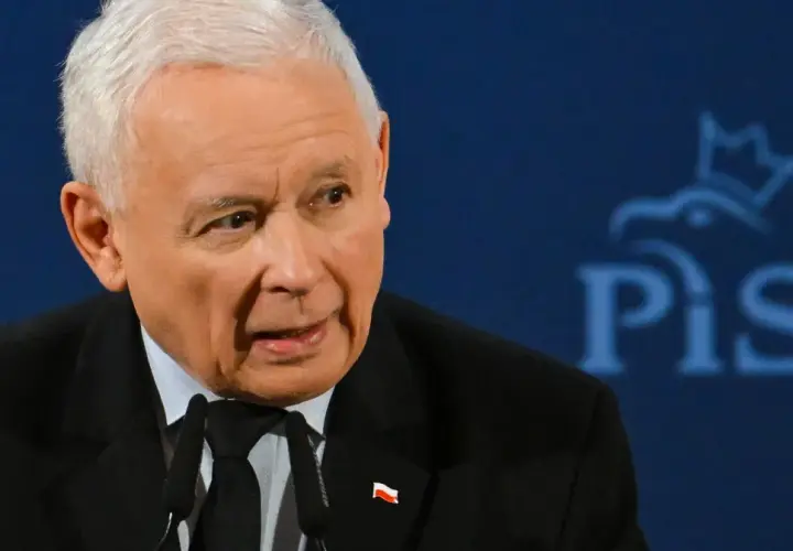 Jarosław Kaczyński, w garniturze z polską flagą, przemawia na tle logo PiS. Czy Jarosław Kaczyński faktycznie planuje oddać władzę młodszym politykom?