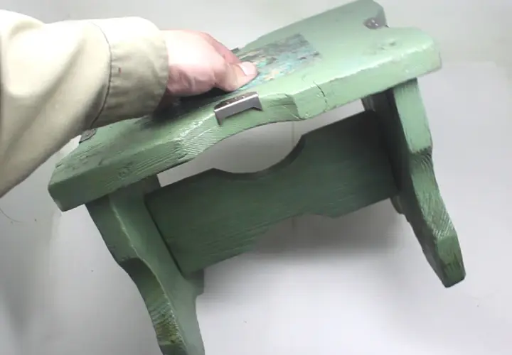 Mano che tiene uno sgabello di legno verde, pronto per verniciare con bomboletta spray.