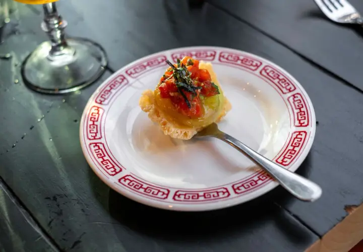 Wykwintny amuse bouche z awokado i pomidorkami na chrupiącym spodzie, podany na talerzyku z czerwonym wzorem.