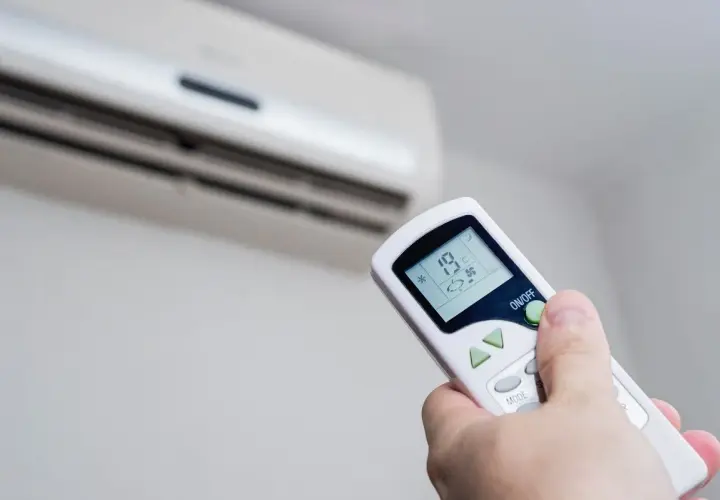 Mando a distancia ajustando la temperatura ideal aire acondicionado para ahorrar energía. Se ve el aire acondicionado y la mano con el control.