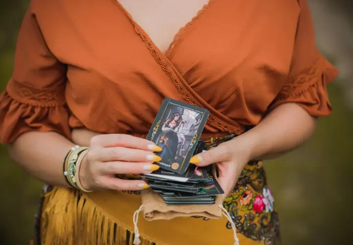 Kobieta trzyma talię kart, jedną z nich jest koło fortuny tarot.