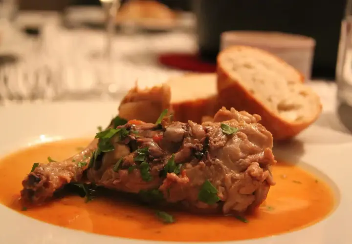 Un plat savoureux de viande mijotée, garni de persil frais, servi avec du pain. Parfait pour accompagner un osso bucco.