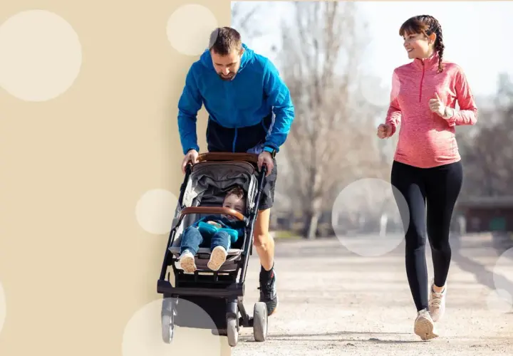 Szczęśliwa kobieta w ciąży biegnie, podczas gdy jej partner pcha wózek z dzieckiem. Aktywność fizyczna w ciąży to świetny pomysł.