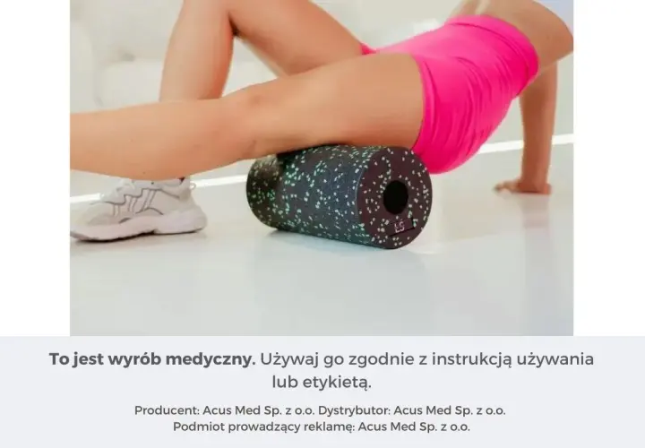 Kobieta wykonuje rolowanie mięśni ud za pomocą czarnego wałka z zielonymi kropkami.