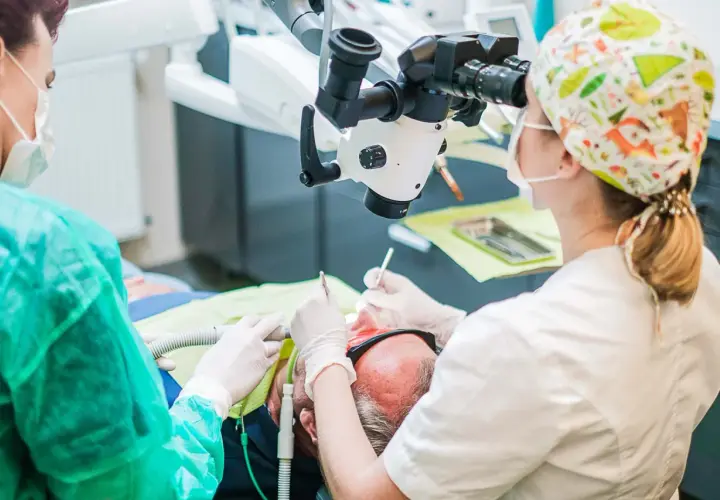 Stomatolog pod mikroskopem aplikuje lekarstwo w zębie pacjenta.
