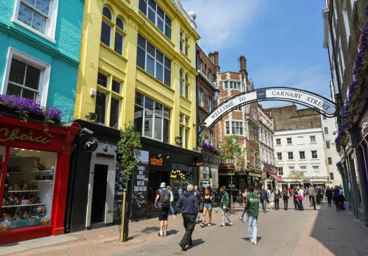Kolorowe fasady sklepów i łuk z napisem "Welcome to Carnaby Street" zapraszają do tętniącej życiem ulicy pełnej ludzi.