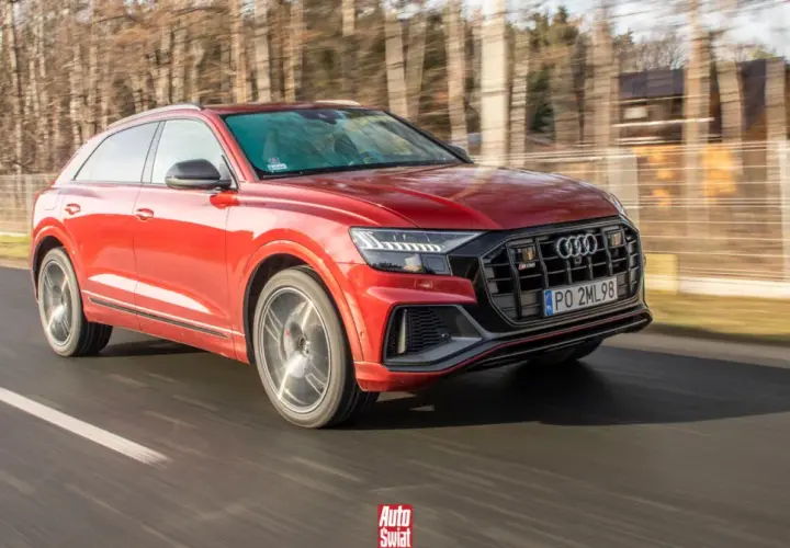 Czerwone Audi SQ8 pędzi po drodze, otoczone rozmazanym lasem.