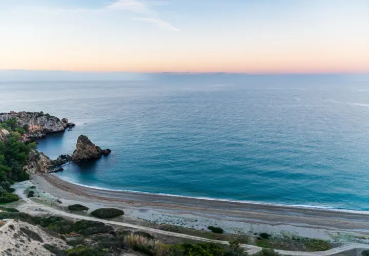 Vista aérea de una cala rocosa y una playa de guijarros en las playas de Málaga al amanecer.