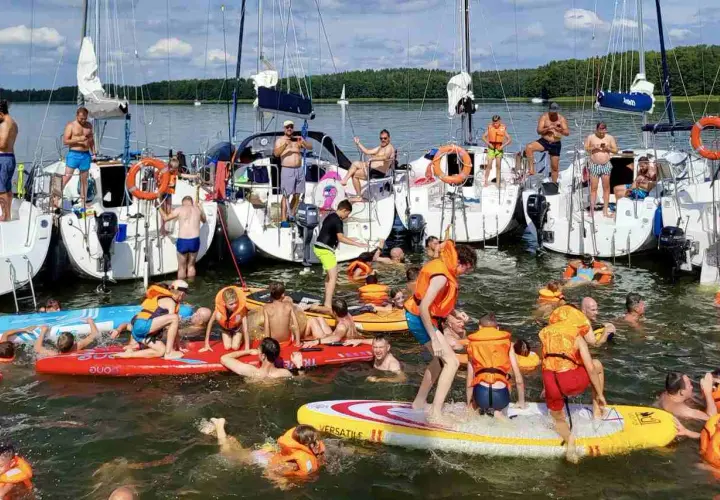 Ludzie w kamizelkach ratunkowych i strojach kąpielowych pływają i bawią się na deskach wodnych przy żaglówkach. Idealny długi weekend czerwiec na wodzie!