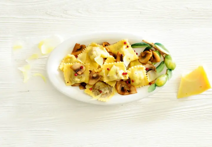 Pyszne ravioli z grzybami, posypane parmezanem i różowym pieprzem, podane na talerzu z gałązką oliwną.