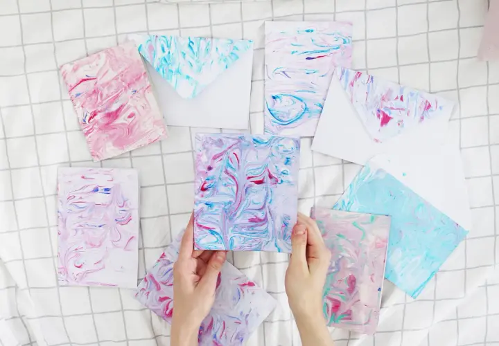 Bunte Karten und Umschläge mit Marmorierungsmuster, die an fließendes Wasser erinnern. Papier marmorieren ist eine kreative Technik.