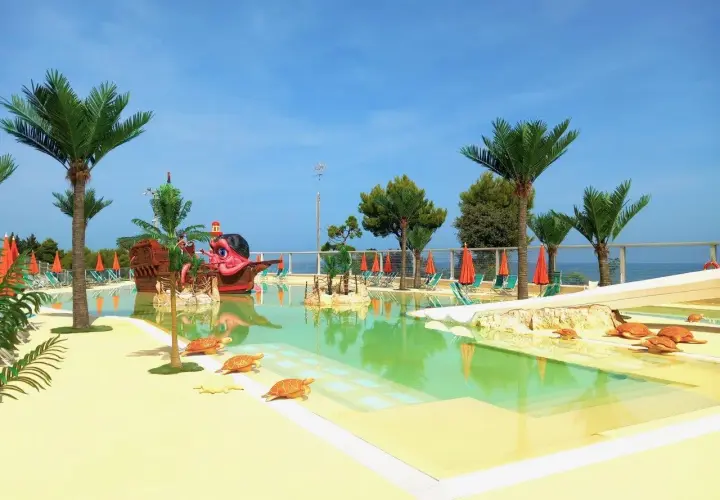 Villaggi Marche sul mare per bambini: piscina con nave pirata, palme e tartarughe. Ideale per vacanze spensierate.