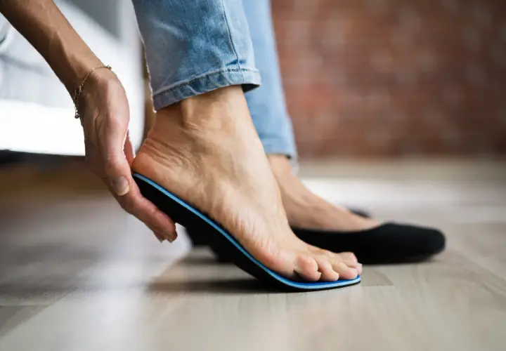 Frau zieht Einlage aus dem Schuh, um Schmerzen nach dem Tragen von Einlagen zu lindern.