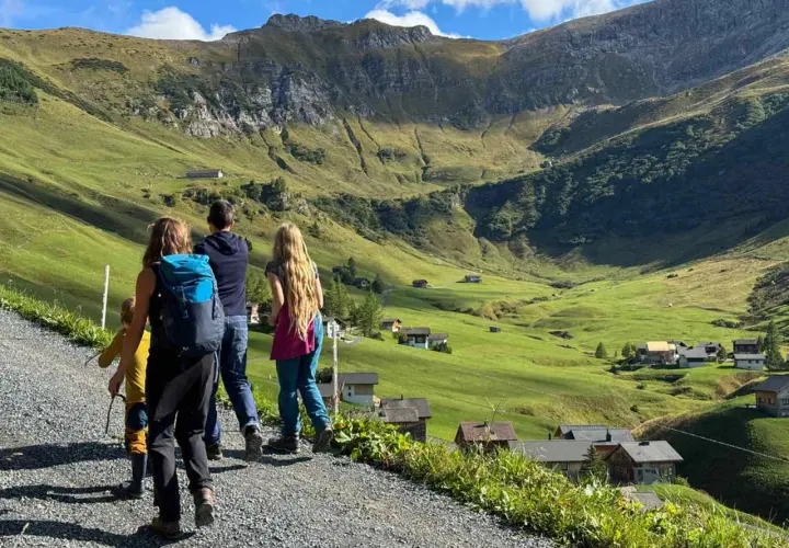 Familie genießt das Liechtenstein wandern in den Alpen. Grüne Hänge, kleine Häuser und ein majestätischer Berg im Hintergrund.
