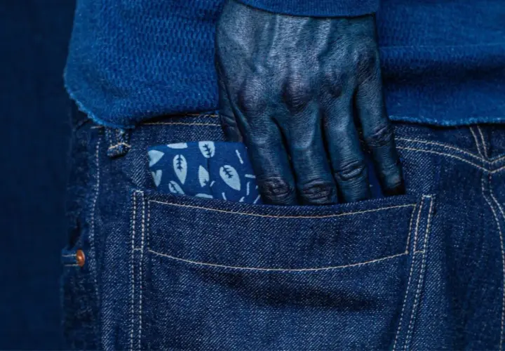Main bleue, main plongée dans la poche d'un jean, le tissu orné de feuilles, témoignage de la teinture.