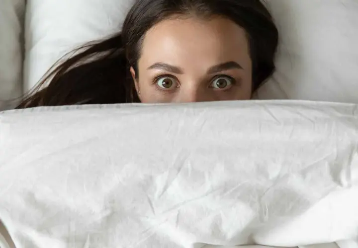 Occhi spalancati sotto le coperte, un'espressione di pura paura di dormire.