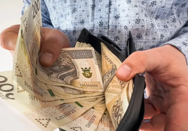 Ręce trzymają portfel z banknotami 200 zł. To może być symbol nagród jubileuszowych w PKP PLK, zasłużona gratyfikacja za lata pracy.