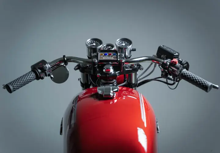 Manubrio di una moto custom rossa con specchietti, tachimetro e contagiri.