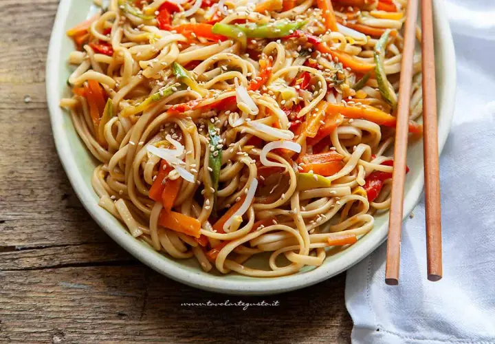 Noodles con verdure colorate, carote, peperoni e germogli di soia, guarniti con semi di sesamo.