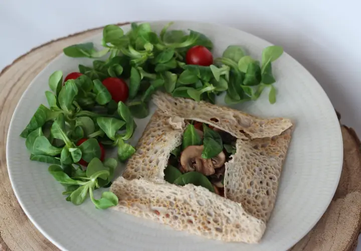 Une galette bretonne garnie de champignons et d'épinards, accompagnée d'une salade verte et de tomates cerises. Un délice pour accompagner un verre de vin.