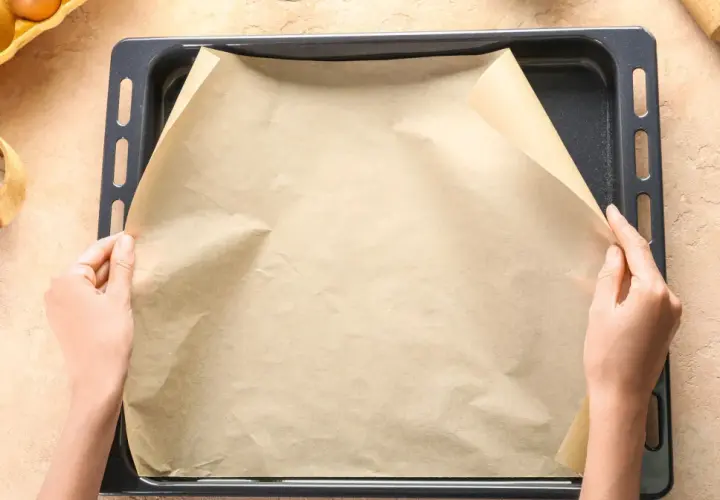 Dłonie układają papier do pieczenia na blasze.