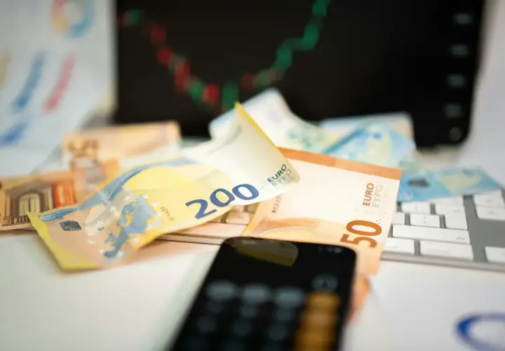 Euro banknoty na klawiaturze, telefon i wykres giełdowy sugerują, jak inwestować w waluty.