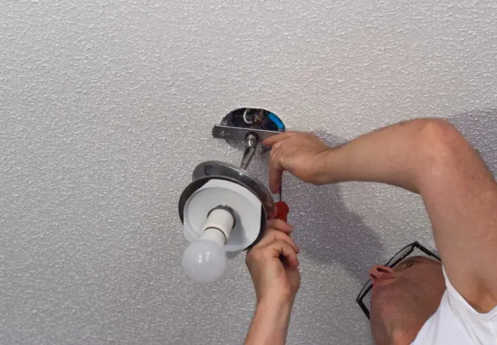 Un homme effectue le branchement d'une lampe au plafond, utilisant un tournevis pour fixer le luminaire.