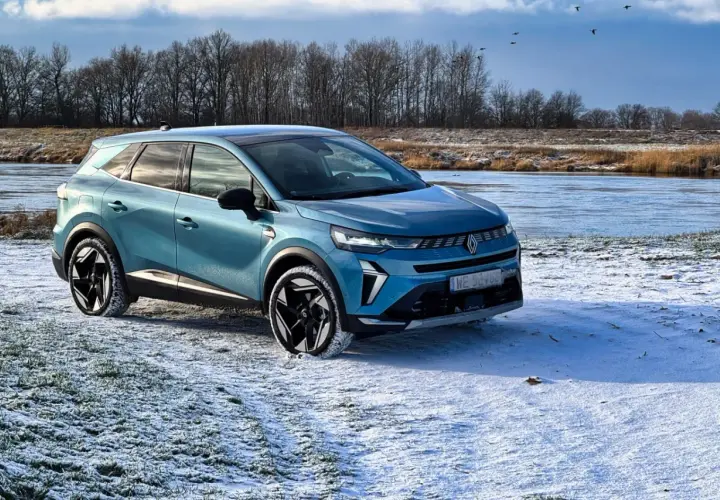 Niebieski Renault Symbioz zaparkowany na zaśnieżonej polanie nad zamarzniętą rzeką.