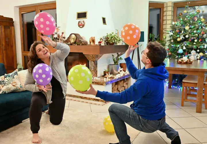 Wesołe pomysły na gry w domu: para bawi się balonami w salonie przy choince.