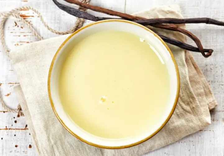 Un bol de crème anglaise onctueuse, prêt à être dégusté, avec des gousses de vanille à proximité.