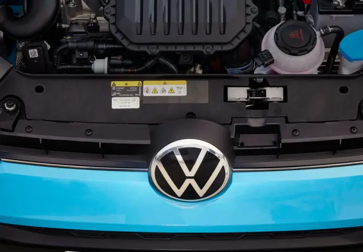 Motorutrymmet på en blå Volkswagen. En etikett visar information om olja och kylvätska, vilket kan vara relevant vid ett **volkswagen gasbil problem**.