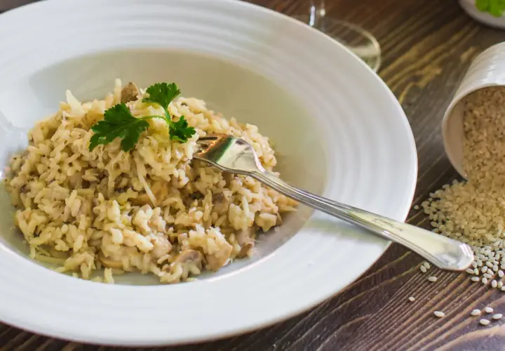 Un cremoso risotto con champiñones y queso parmesano, listo para disfrutar. Al lado, un cuenco volcado con arroz para risotto.