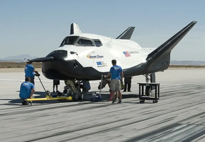 Dream Chaser, kosmiczny pojazd, przygotowywany do startu. Zespół techników pracuje przy jego podwoziu na pustynnym lotnisku.