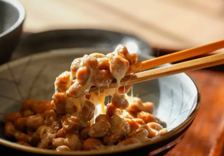 Natto chinasi: attenzione alle controindicazioni. Un primo piano di natto appiccicoso sollevato da bacchette.