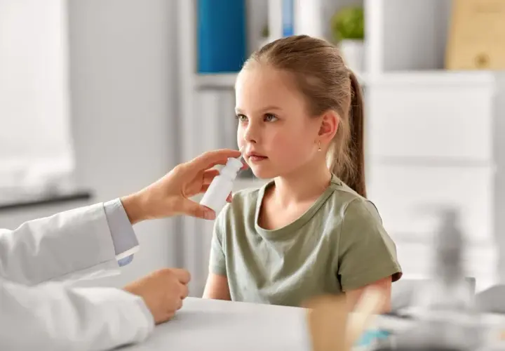 Niña recibe spray nasal para aliviar síntomas de rinitis alérgica. El doctor investiga las causas.