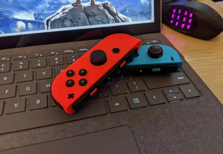 Czerwony i niebieski Joy-Con na klawiaturze laptopa, gotowe do gry. Dowiedz się, jak podłączyć Nintendo do komputera.