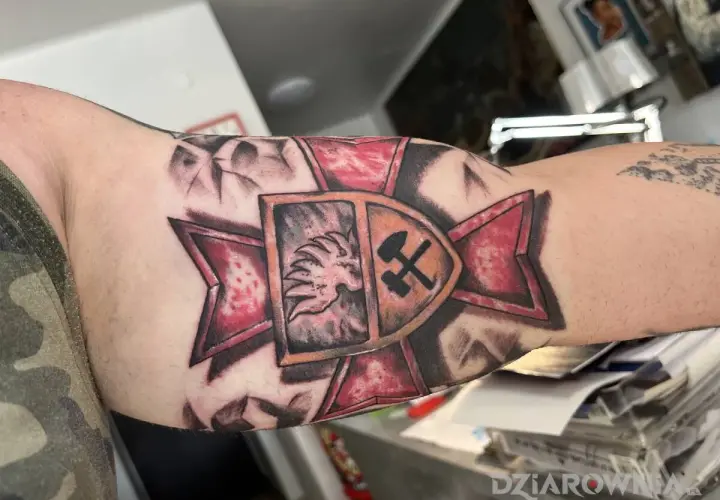 Tatuaż patriotyczny na ramieniu: lew w koronie i skrzyżowane młot i kilof na tle czerwonej gwiazdy.