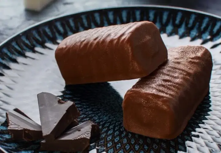 Dwa czekoladowe batony proteinowe na talerzu z kawałkami gorzkiej czekolady. Idealne do domowego przepisu na batony proteinowe.