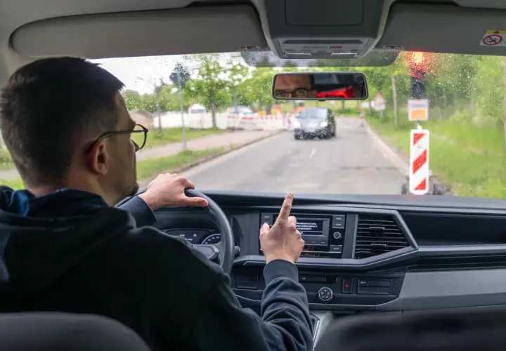 Kierowca w okularach wskazuje palcem na ekran nawigacji, gdy zbliża się do drogi dla pieszych.