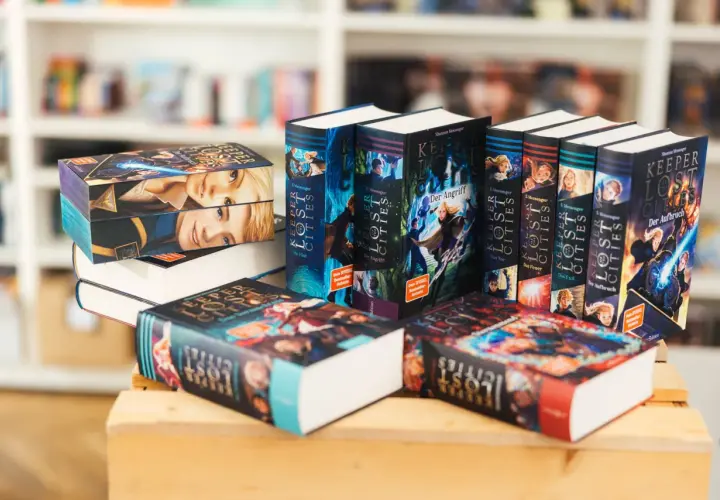 Stapel von "Keeper of the Lost Cities" Büchern, eine beliebte Fantasy-Buchreihe für Erwachsene, mit farbenfrohen Covern und Illustrationen.
