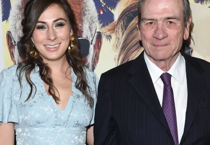 Tommy Lee Jones z żoną, uśmiechnięci na tle plakatu filmowego.
