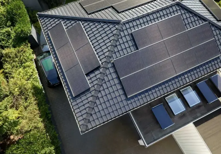 Dach mit Solarmodulen, ein schwarzes Auto und grüne Bäume. Die **agri pv voraussetzungen** sind erfüllt für dieses sonnenbeschienene Haus.