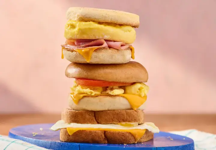 Une pile de sandwichs gourmands, parfaits pour une recette de petit-déjeuner. Œufs brouillés, fromage fondant, jambon et tomate.