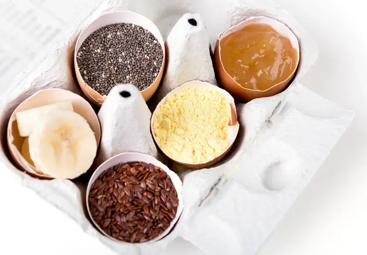 Dans une boîte à œufs, des alternatives pour remplacer les œufs : graines de chia, compote de pommes, farine de pois chiche, graines de lin, rondelles de banane.