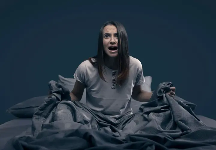 Mujer en la cama, con expresión de angustia, sujetando las sábanas. Parece que se despierta sobresaltada porque me encuentro mal por las mañanas.