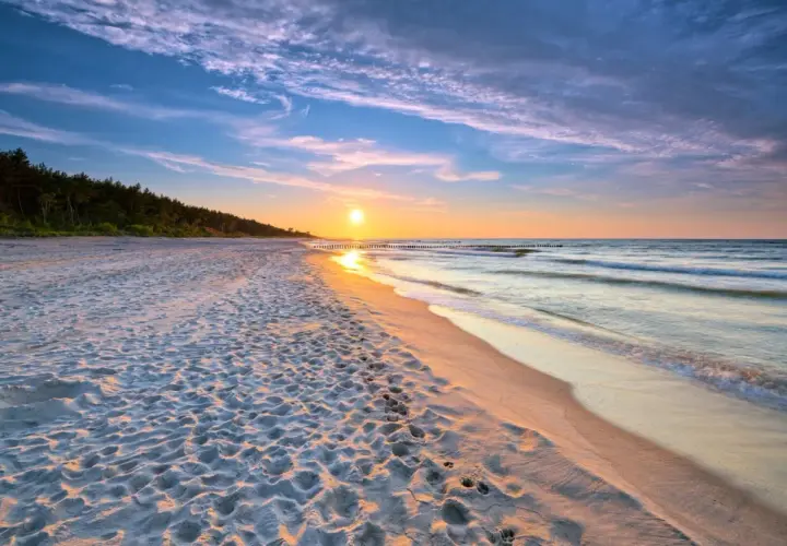 Zachód słońca nad morzem, piaszczysta plaża z odciskami stóp, las w tle. Idealne, fajne miejsce nad morzem dla dwojga na romantyczny spacer.