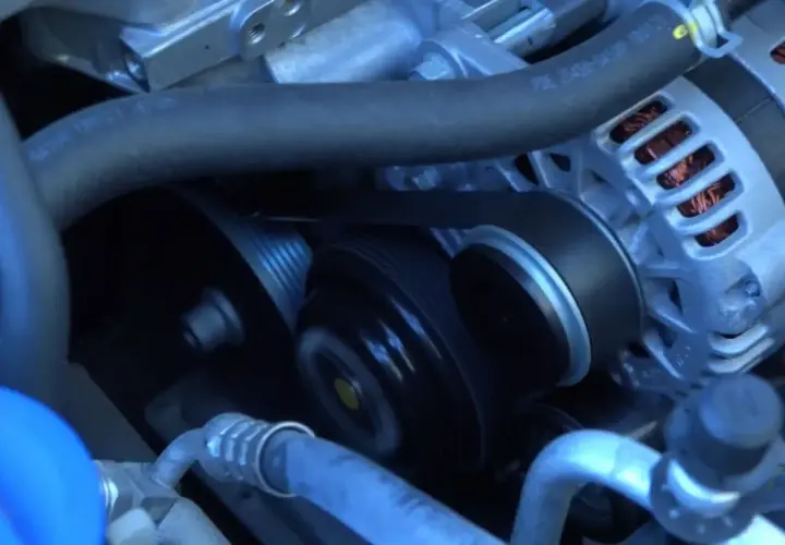 La correa de distribución se ve girando en el motor, conectando el alternador y otras poleas.