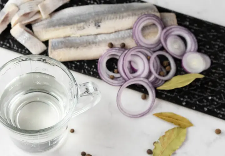Förberedelser för inlagd sill: sillfiléer, rödlök, lagerblad, pepparkorn och en bägare med ättika. 1, 2, 3 lag.
