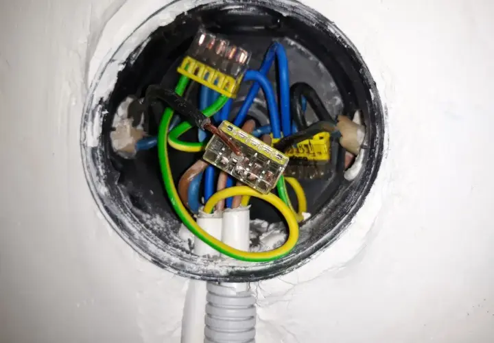 Widać przewody elektryczne w puszce, przygotowane do zerowania gniazdka. Zielono-żółty przewód ochronny jest widoczny.